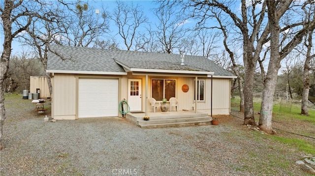 view of front of home with covered porch, a shingled roof, gravel driveway, and a garage