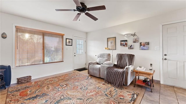 sitting room featuring baseboards, ceiling fan, and a wood stove