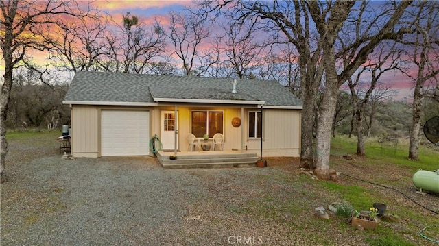 view of front of house featuring covered porch, gravel driveway, a garage, and roof with shingles