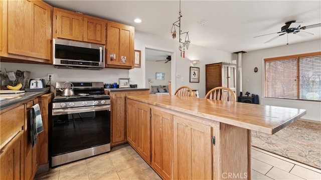 kitchen featuring light tile patterned floors, a peninsula, ceiling fan, stainless steel appliances, and a kitchen breakfast bar