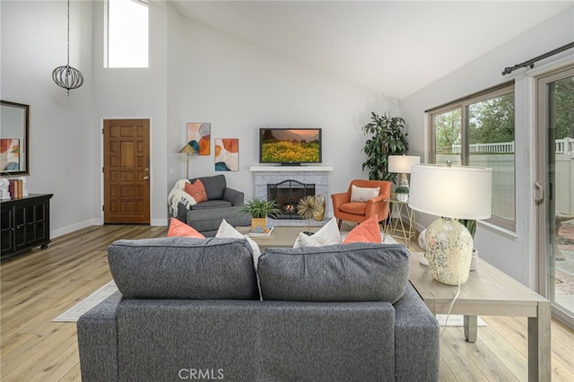 living room with baseboards, high vaulted ceiling, a brick fireplace, and wood finished floors