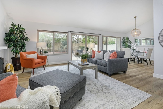 living room featuring hardwood / wood-style floors, lofted ceiling, baseboards, and an inviting chandelier