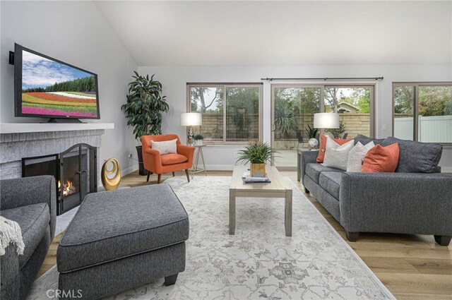 living area featuring plenty of natural light, wood finished floors, a fireplace, and vaulted ceiling