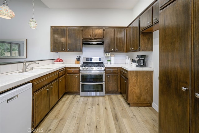 kitchen with under cabinet range hood, dishwasher, double oven range, light wood-style floors, and a sink