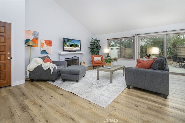 living area with a brick fireplace, baseboards, light wood-type flooring, and high vaulted ceiling