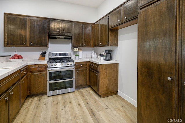 kitchen featuring tile countertops, range with two ovens, light wood-style flooring, dark brown cabinetry, and under cabinet range hood