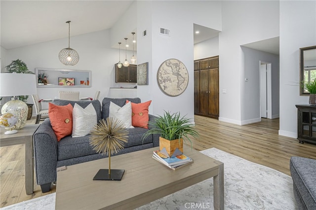 living area with visible vents, high vaulted ceiling, light wood-type flooring, and baseboards