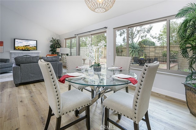 dining area with baseboards, light wood-style floors, and vaulted ceiling