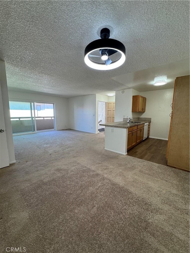 unfurnished living room featuring a sink, a textured ceiling, baseboards, and dark colored carpet