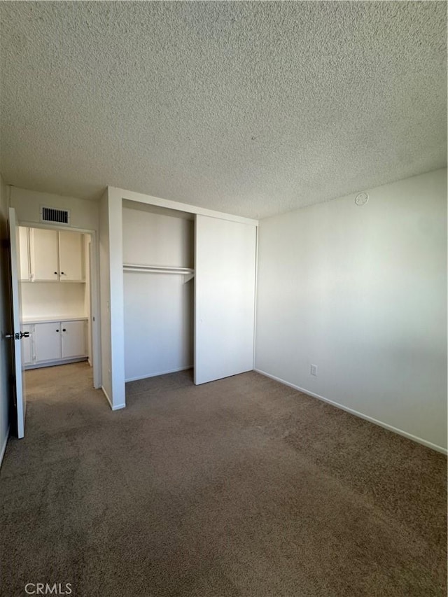 unfurnished bedroom with visible vents, a textured ceiling, a closet, and carpet flooring