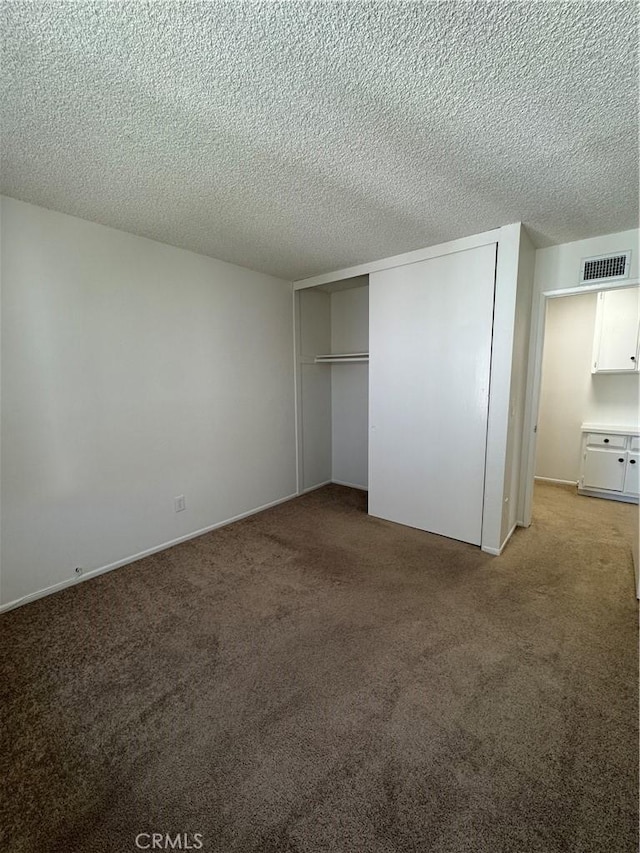 unfurnished bedroom featuring visible vents, light carpet, a textured ceiling, and a closet