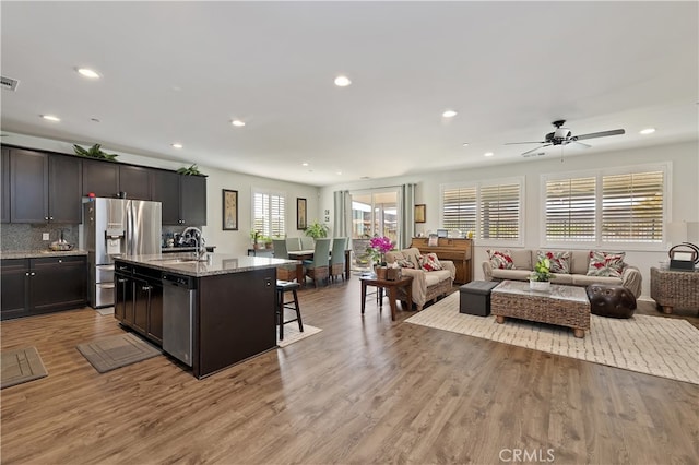 kitchen featuring light stone countertops, light wood finished floors, stainless steel appliances, a kitchen breakfast bar, and open floor plan