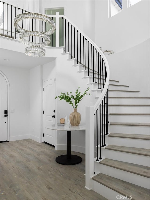 interior space featuring stairs, a chandelier, wood finished floors, and a towering ceiling