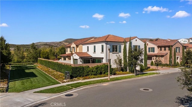 mediterranean / spanish house featuring stucco siding, a mountain view, a front lawn, and a tiled roof