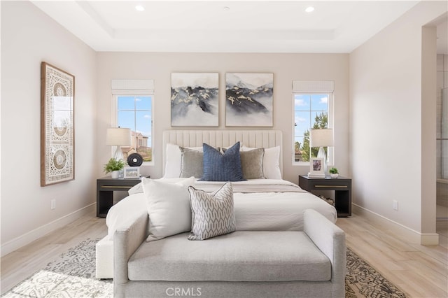 bedroom featuring light wood finished floors, baseboards, and a tray ceiling