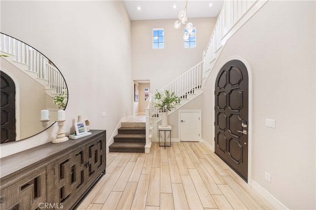 foyer with stairway, baseboards, light wood finished floors, an inviting chandelier, and a towering ceiling