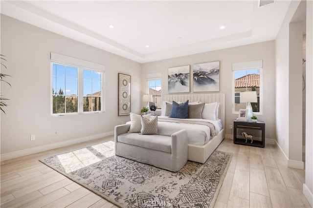 bedroom featuring light wood-type flooring, baseboards, and a raised ceiling