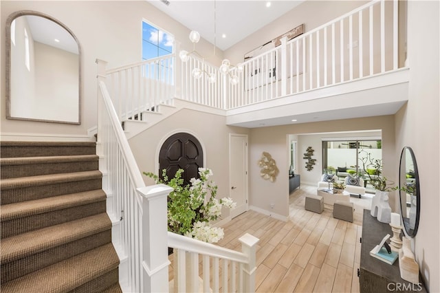 staircase with plenty of natural light, a towering ceiling, an inviting chandelier, and wood finished floors