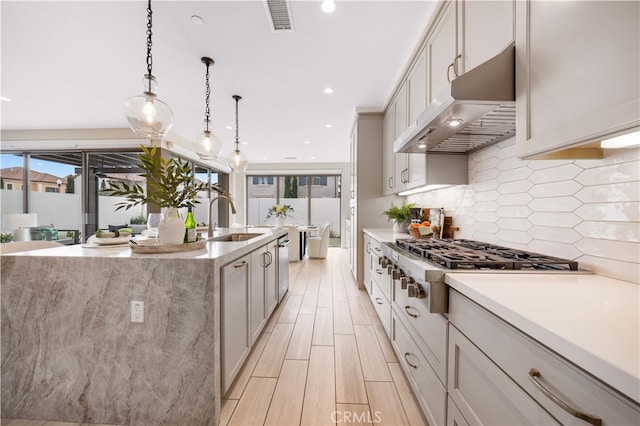 kitchen featuring visible vents, wood tiled floor, a sink, under cabinet range hood, and tasteful backsplash