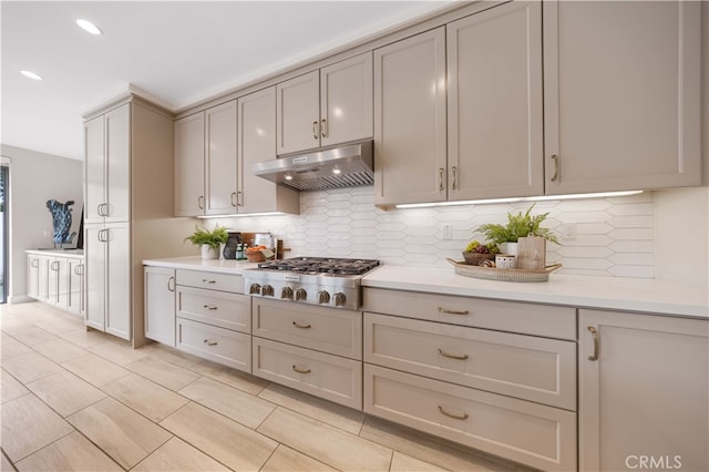 kitchen featuring under cabinet range hood, tasteful backsplash, stainless steel gas stovetop, and light countertops