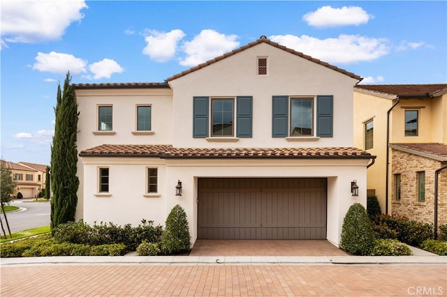 mediterranean / spanish-style house with decorative driveway, an attached garage, and stucco siding