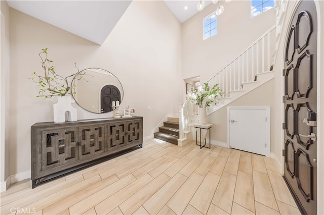 entryway featuring high vaulted ceiling, stairs, baseboards, and wood finished floors