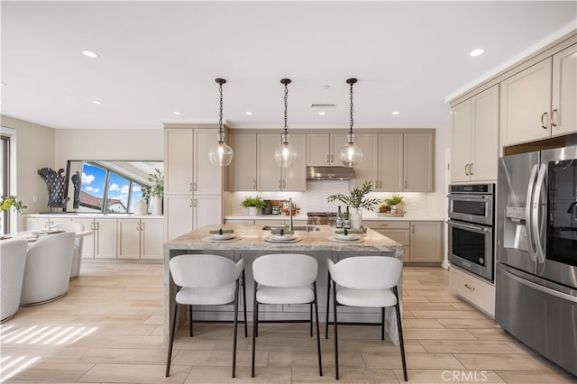 kitchen featuring wood finish floors, a breakfast bar, under cabinet range hood, appliances with stainless steel finishes, and decorative backsplash