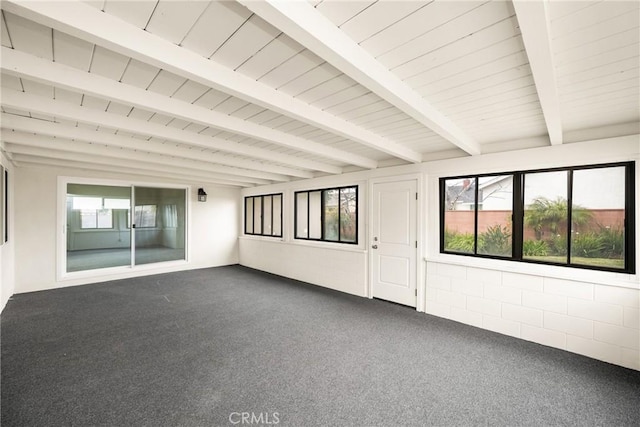 spare room with beamed ceiling, plenty of natural light, and dark carpet