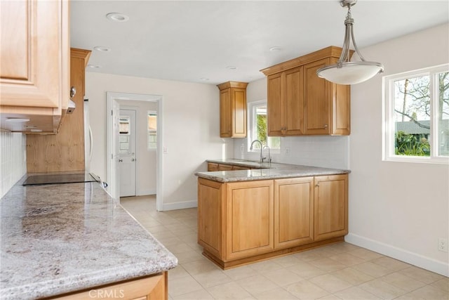 kitchen featuring light stone countertops, a peninsula, a sink, black electric cooktop, and tasteful backsplash