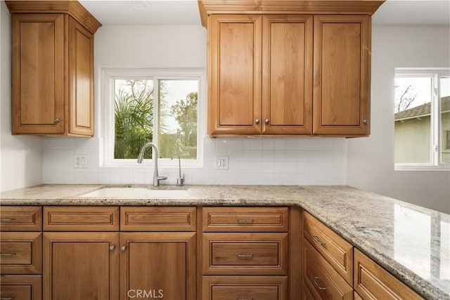 kitchen featuring a sink, brown cabinets, tasteful backsplash, and light stone counters