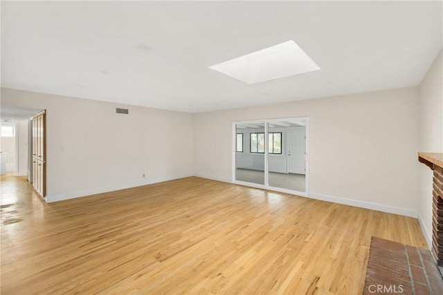 unfurnished living room featuring visible vents, a skylight, light wood-type flooring, and baseboards