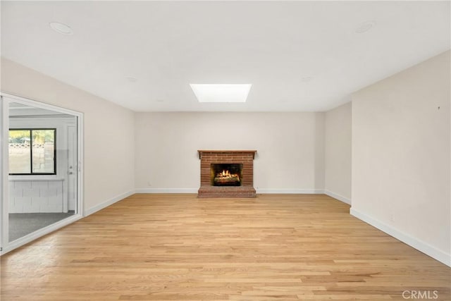 unfurnished living room featuring light wood-style flooring, a fireplace, a skylight, and baseboards