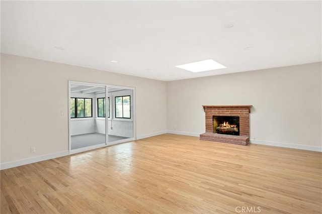 unfurnished living room featuring a fireplace, a skylight, light wood-style floors, and baseboards