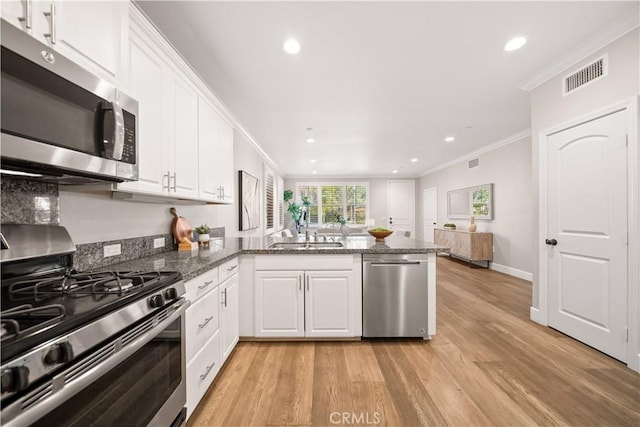 kitchen with visible vents, a peninsula, white cabinets, stainless steel appliances, and a sink