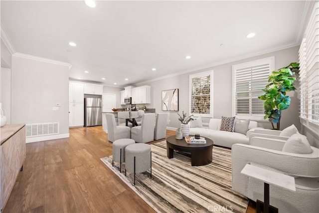 living room featuring recessed lighting, visible vents, light wood-style flooring, and ornamental molding