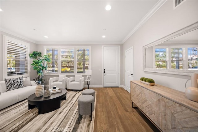 living room with a wealth of natural light, visible vents, wood finished floors, and ornamental molding