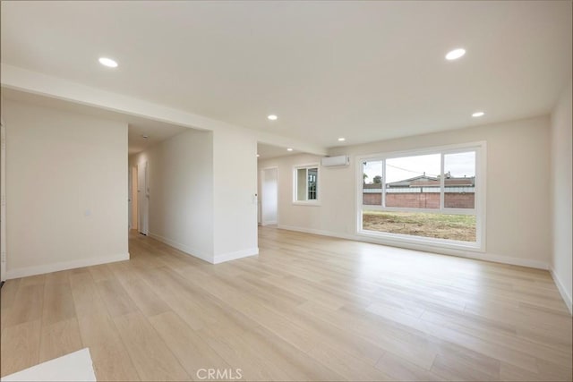 unfurnished living room with recessed lighting, baseboards, an AC wall unit, and light wood finished floors