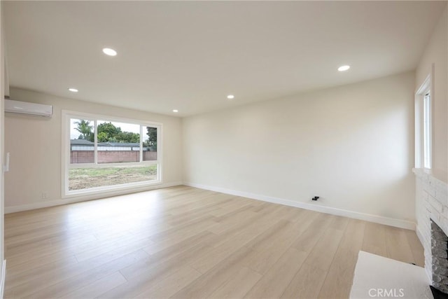 spare room with recessed lighting, light wood-style floors, a fireplace, and a wall unit AC