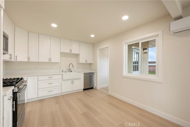 kitchen featuring an AC wall unit, light wood-type flooring, light countertops, appliances with stainless steel finishes, and a sink