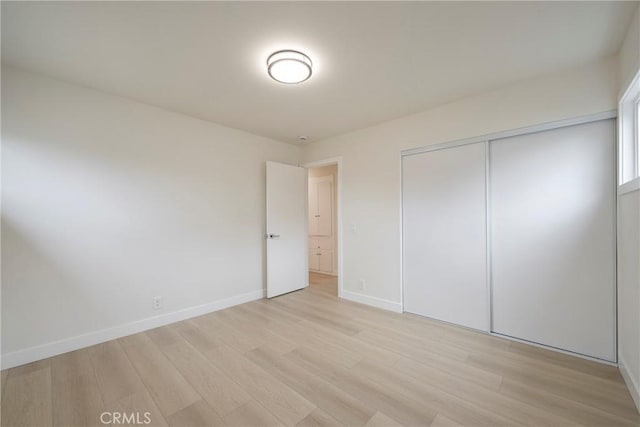 unfurnished bedroom featuring light wood-type flooring, baseboards, and a closet