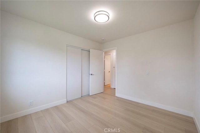 unfurnished bedroom with a closet, baseboards, and light wood finished floors