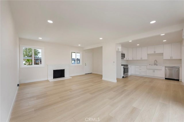 unfurnished living room featuring baseboards, light wood-style flooring, a fireplace, recessed lighting, and a sink