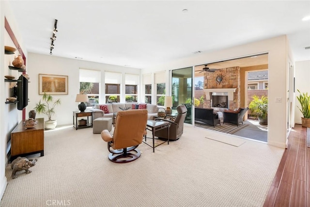 living area with visible vents, track lighting, baseboards, a stone fireplace, and wood finished floors