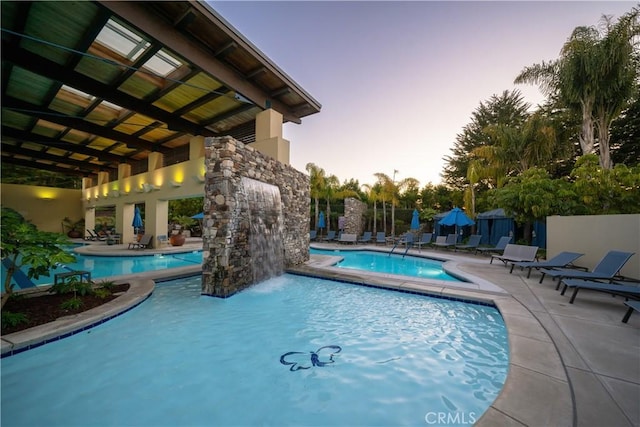 community pool with a patio area, fence, and a hot tub