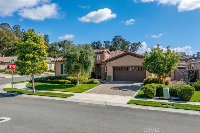 mediterranean / spanish home featuring a front yard, an attached garage, stucco siding, a tile roof, and decorative driveway