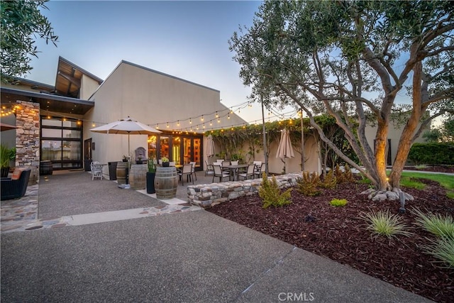 view of front of home with a patio, stone siding, and stucco siding