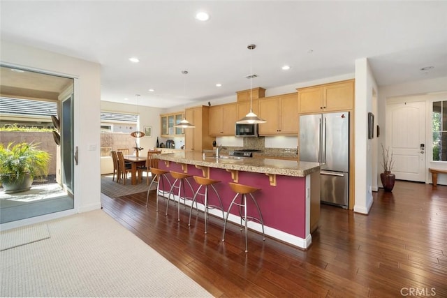 kitchen featuring dark wood-type flooring, a breakfast bar, a kitchen island with sink, recessed lighting, and stainless steel appliances