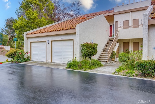 exterior space with stucco siding, a tile roof, stairs, and a garage