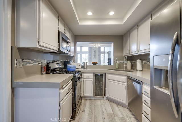 kitchen featuring a sink, stainless steel appliances, wine cooler, light countertops, and a raised ceiling