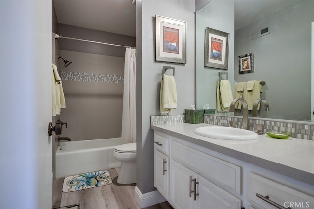 full bathroom with visible vents, shower / bath combo with shower curtain, toilet, wood finished floors, and vanity